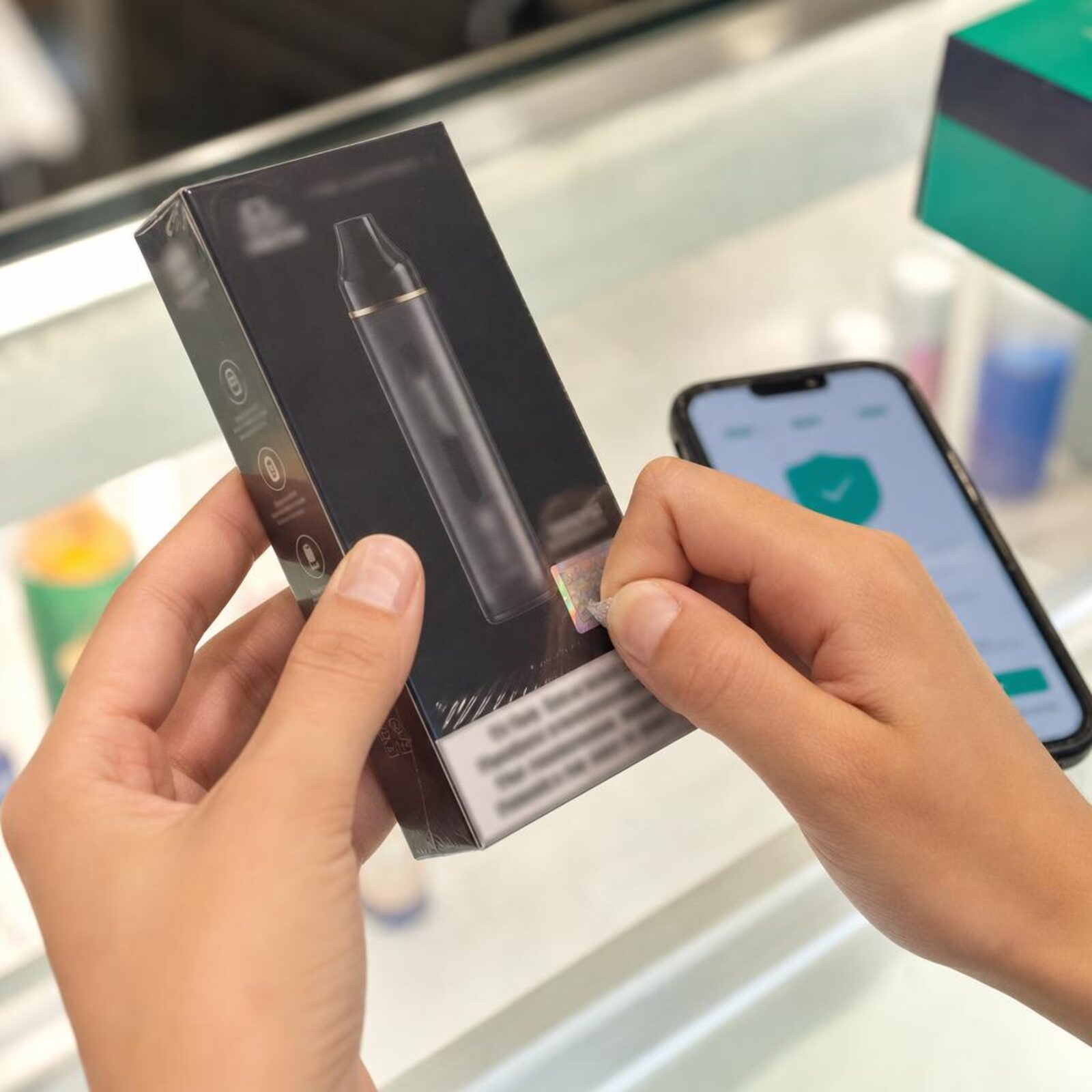 Hands scratching the authentication sticker on a sealed vape box to verify it.